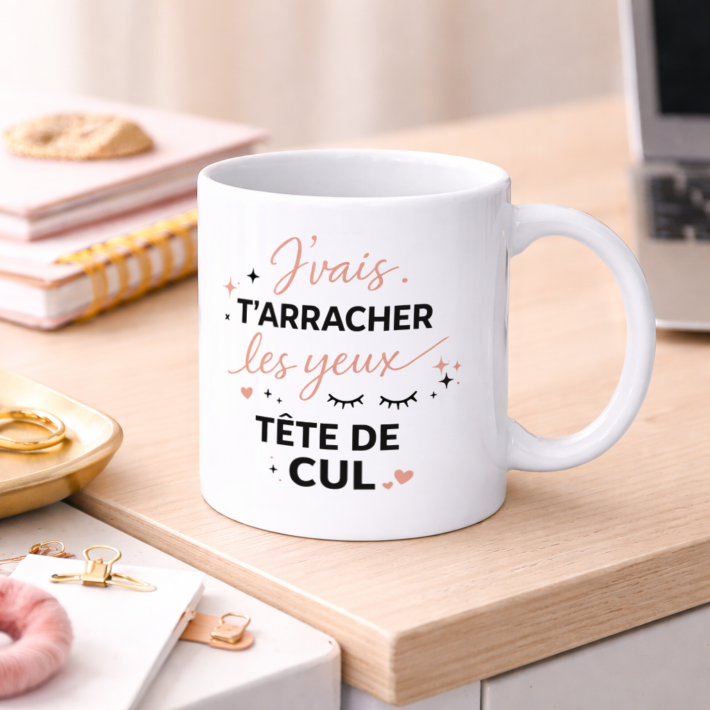Mug blanc en céramique avec inscription humoristique « J’vais t’arracher les yeux tête de cul » posé sur un bureau